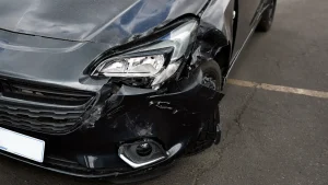Close-up of a damaged car headlight in a parking lot showing cracks and scratches.