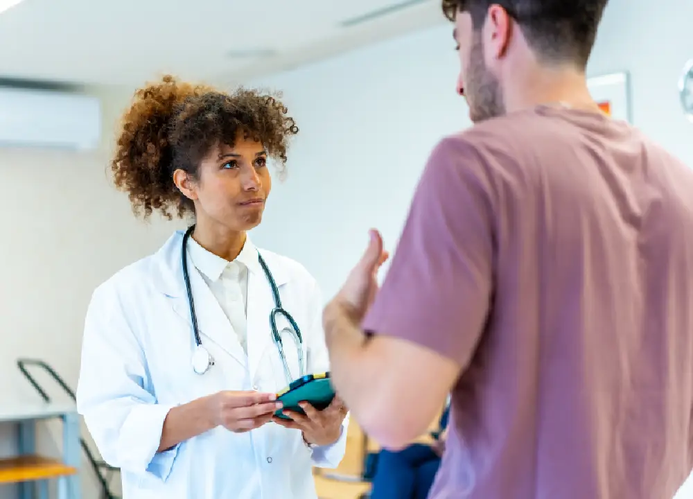 A female doctor attentively listens as a patient explains their symptoms in a hospital setting.