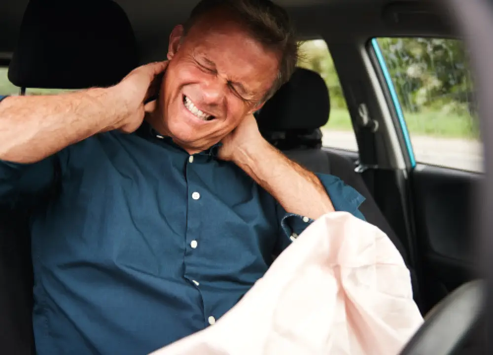 Person sitting in car holding neck in pain after a car accident