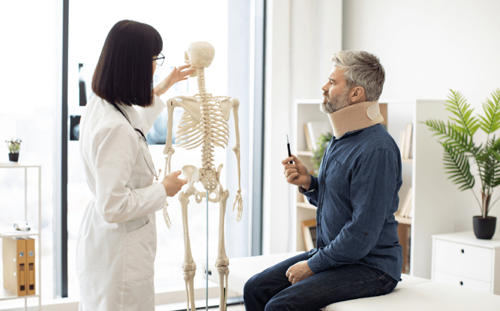 Doctor shows spine model to patient wearing a neck brace